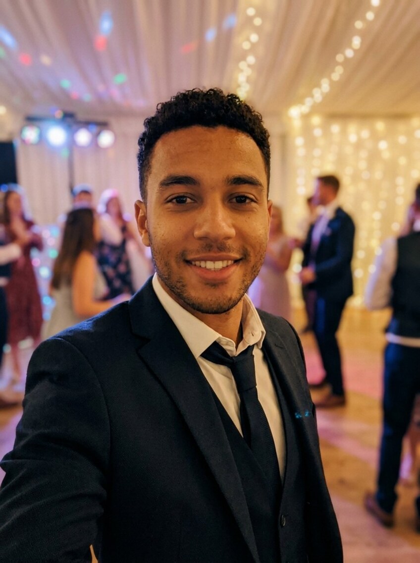 A guest in a black suit on the marquee dancefloor, a curtain of fairy lights and coloured spots behind him